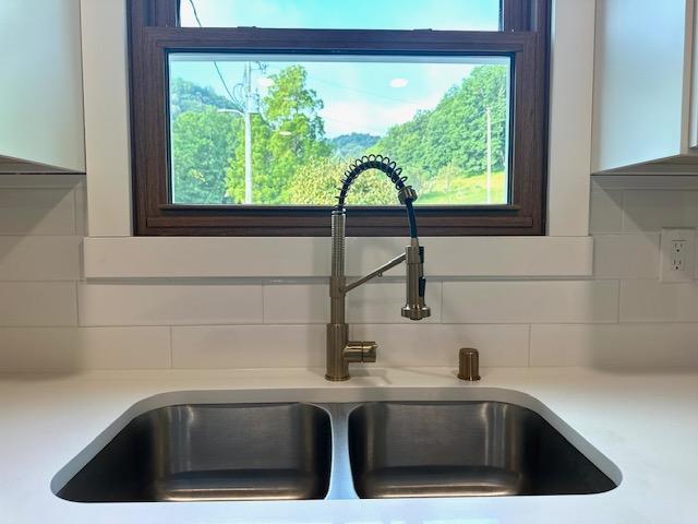 room details featuring tasteful backsplash, white cabinetry, light countertops, and a sink