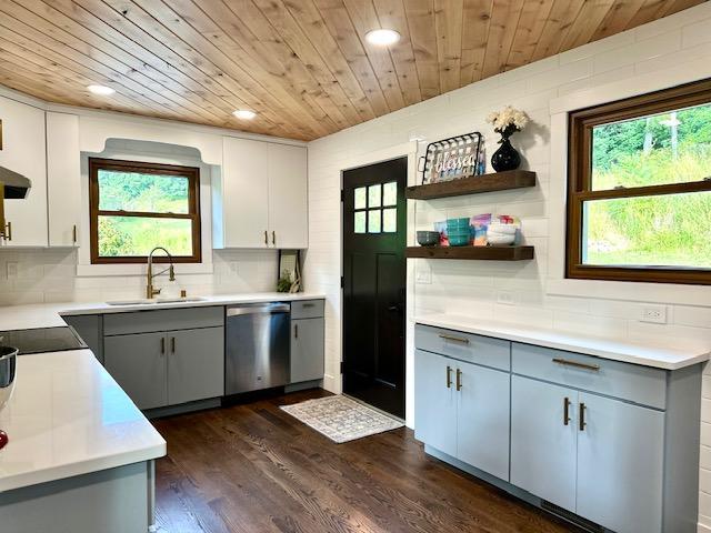 kitchen featuring gray cabinets, light countertops, stainless steel dishwasher, a sink, and wooden ceiling