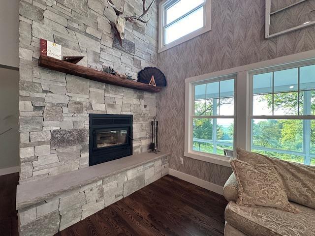 living room with dark wood-style flooring, a stone fireplace, and baseboards