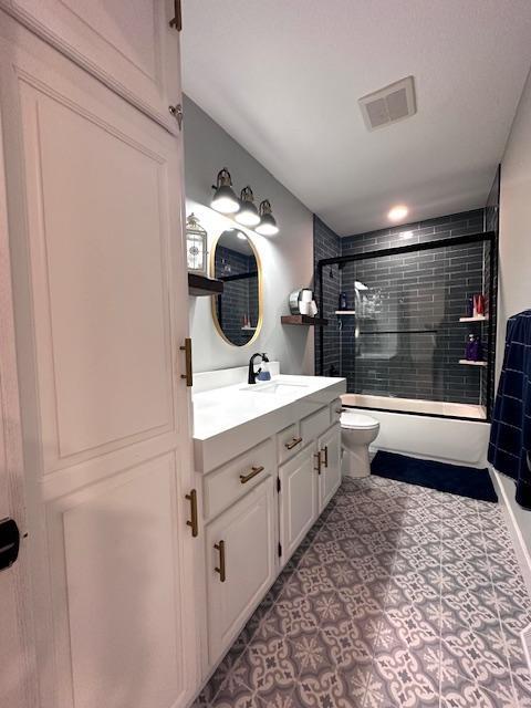 full bathroom featuring toilet, enclosed tub / shower combo, visible vents, and vanity