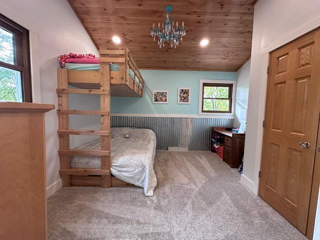 unfurnished bedroom with light colored carpet, wooden ceiling, a wainscoted wall, vaulted ceiling, and a notable chandelier