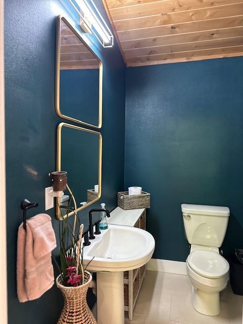 half bathroom featuring wooden ceiling, baseboards, toilet, and tile patterned floors