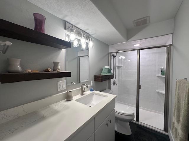 full bathroom with a textured ceiling, toilet, vanity, visible vents, and a stall shower