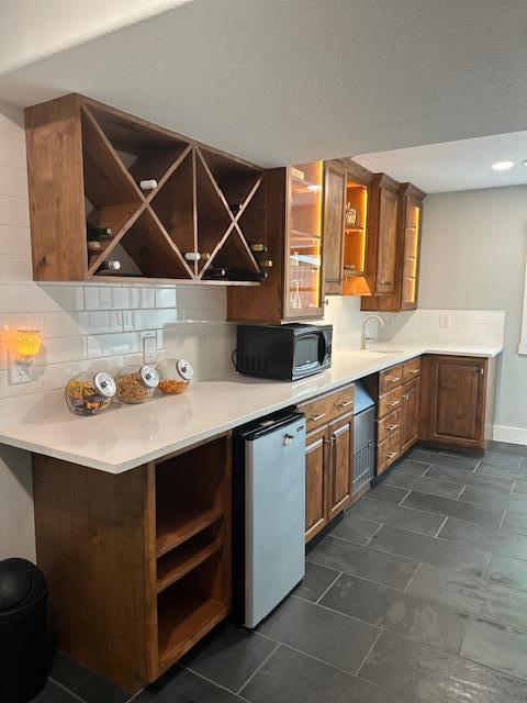 kitchen with open shelves, tasteful backsplash, light countertops, black microwave, and a peninsula