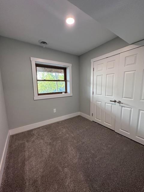 unfurnished bedroom with a closet, visible vents, dark carpet, and baseboards