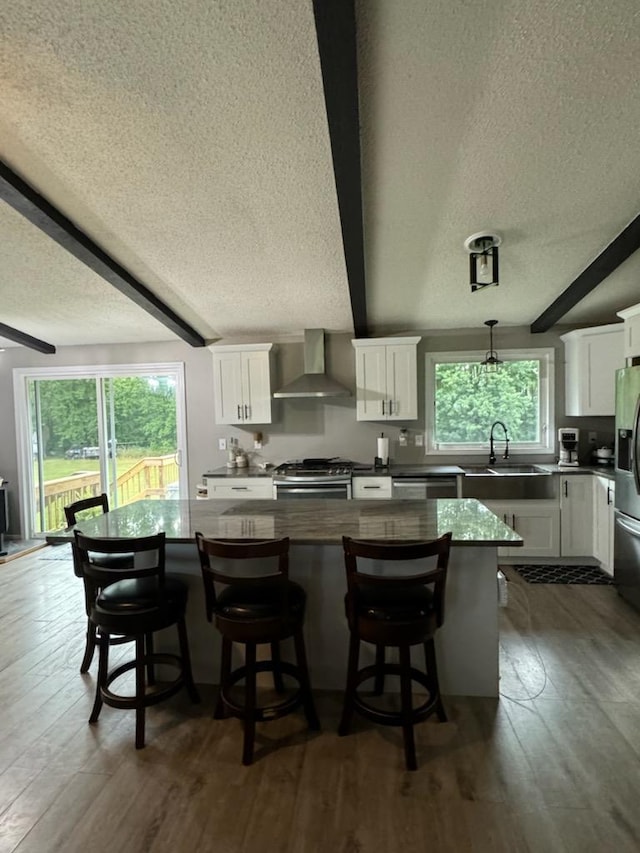 kitchen featuring plenty of natural light, a kitchen island, stainless steel appliances, wall chimney range hood, and beam ceiling