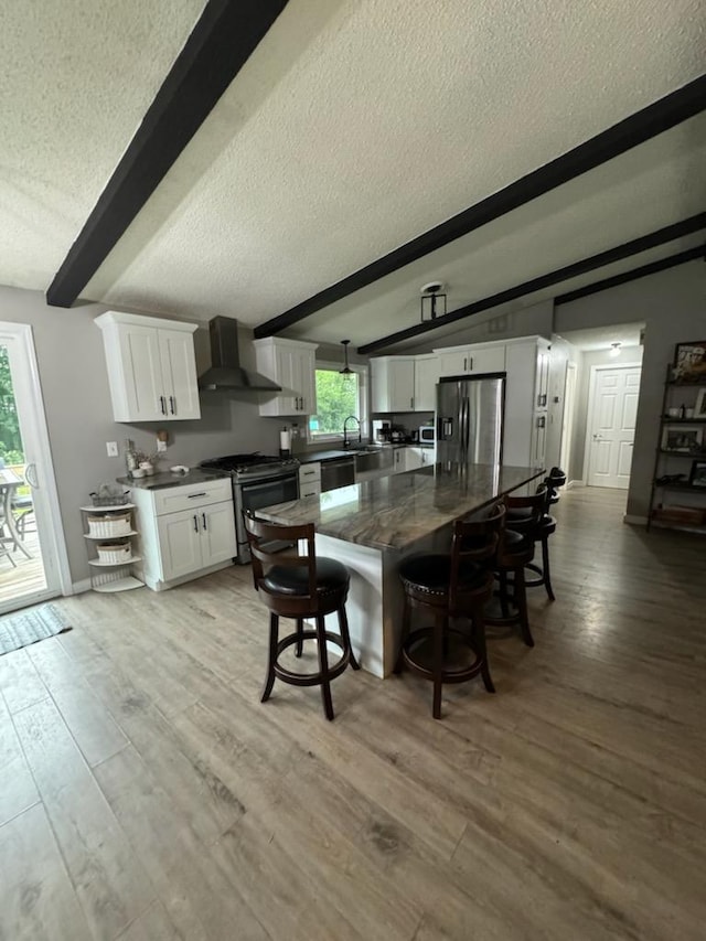 kitchen featuring stainless steel appliances, a sink, white cabinetry, wall chimney range hood, and a kitchen bar