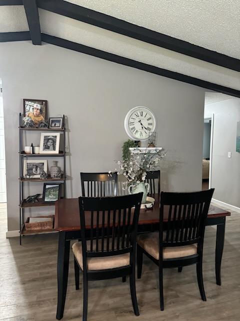 dining room featuring a textured ceiling, lofted ceiling with beams, and wood finished floors