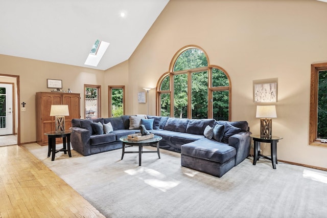 living room with light hardwood / wood-style floors, high vaulted ceiling, a skylight, and a healthy amount of sunlight