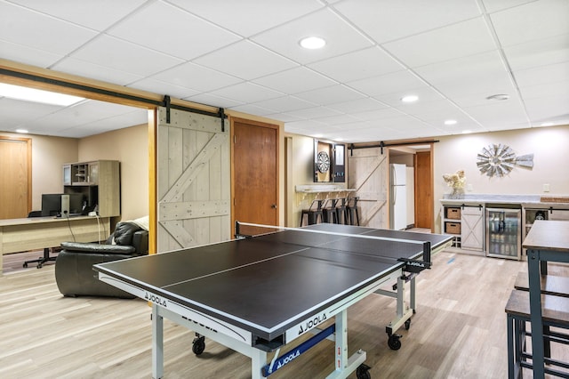 game room with a paneled ceiling, light hardwood / wood-style floors, wine cooler, and a barn door