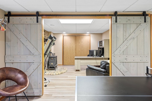 basement featuring a barn door, hardwood / wood-style flooring, and a paneled ceiling