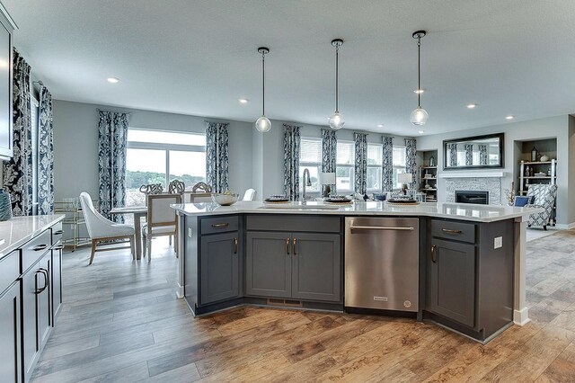 kitchen featuring hanging light fixtures, a kitchen island with sink, dishwasher, a stone fireplace, and sink