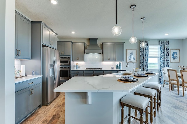 kitchen featuring an island with sink, premium range hood, a kitchen bar, light hardwood / wood-style floors, and stainless steel appliances