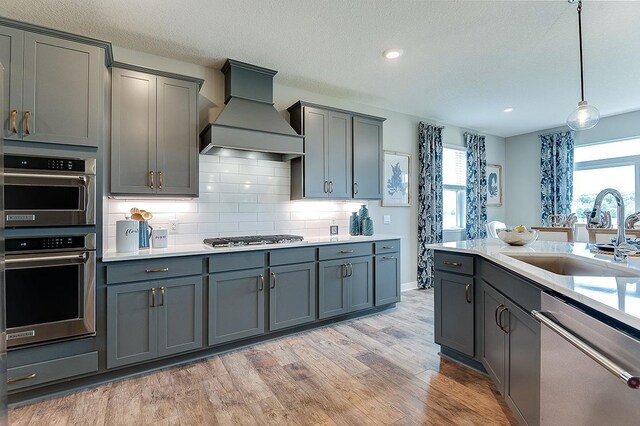 kitchen featuring sink, gray cabinets, custom exhaust hood, appliances with stainless steel finishes, and light hardwood / wood-style floors