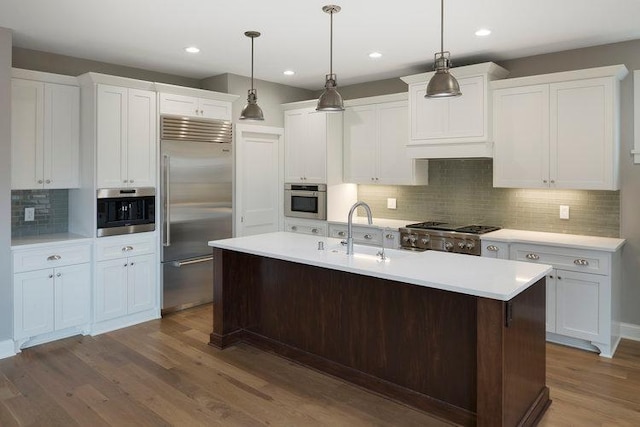 kitchen with hardwood / wood-style floors, decorative backsplash, appliances with stainless steel finishes, a center island with sink, and white cabinets