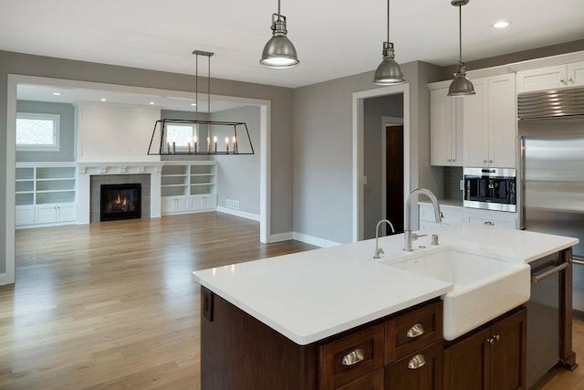 kitchen with a tiled fireplace, light hardwood / wood-style flooring, an island with sink, sink, and appliances with stainless steel finishes