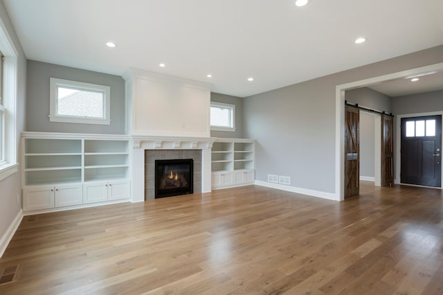 unfurnished living room featuring a barn door, a fireplace, and light hardwood / wood-style flooring