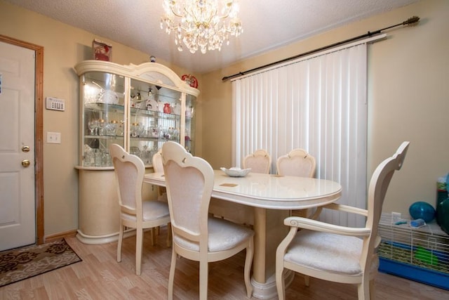 dining space featuring light wood-type flooring, a textured ceiling, and a notable chandelier