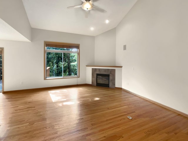 unfurnished living room with light wood-type flooring, vaulted ceiling, a tiled fireplace, and ceiling fan