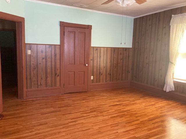 empty room featuring wood walls, ceiling fan, light wood-style floors, and ornamental molding