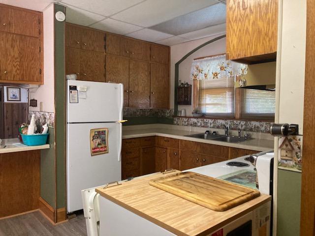 kitchen with wood finished floors, freestanding refrigerator, a sink, light countertops, and a paneled ceiling