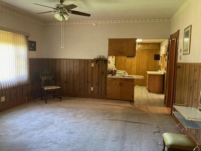 unfurnished room with ceiling fan, light colored carpet, wood walls, and wainscoting