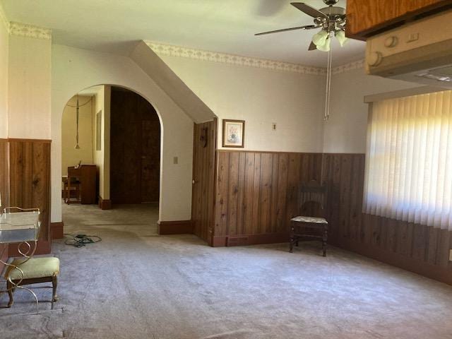 bonus room featuring carpet, a wainscoted wall, a ceiling fan, arched walkways, and wood walls