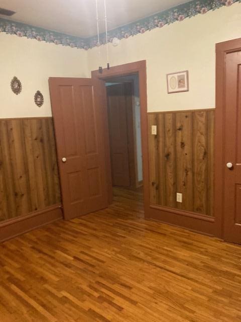 spare room with visible vents, wooden walls, wood finished floors, and a wainscoted wall