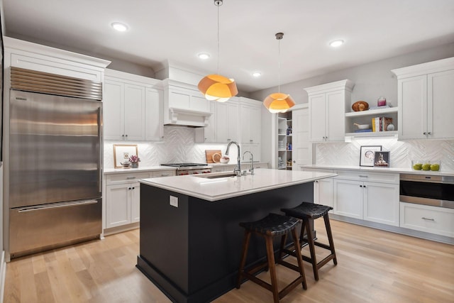 kitchen with sink, hanging light fixtures, built in fridge, white cabinets, and light wood-type flooring