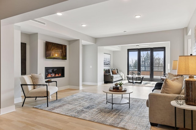 living area featuring visible vents, baseboards, a glass covered fireplace, and light wood-style flooring