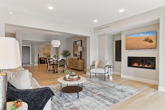 living area with visible vents, light wood-style flooring, a glass covered fireplace, recessed lighting, and baseboards