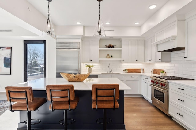 kitchen with a kitchen bar, premium appliances, a center island, light hardwood / wood-style floors, and white cabinetry