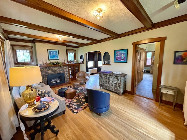 living room featuring a textured ceiling, a tile fireplace, hardwood / wood-style floors, and beamed ceiling