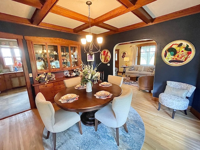 dining room featuring coffered ceiling, beamed ceiling, light wood-type flooring, and an inviting chandelier