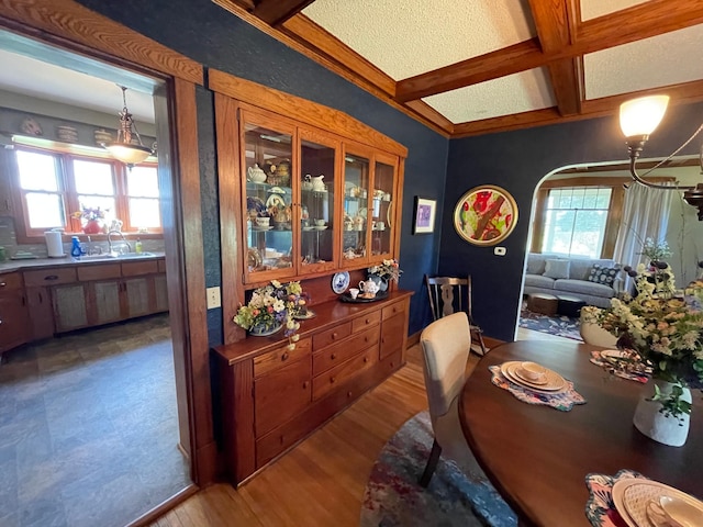 dining area with light wood-type flooring, coffered ceiling, beamed ceiling, and plenty of natural light