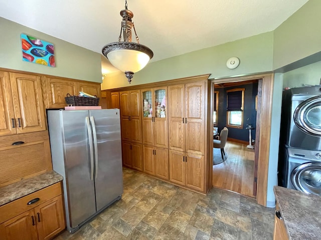 kitchen with stacked washer / drying machine, hanging light fixtures, dark wood-type flooring, and stainless steel refrigerator