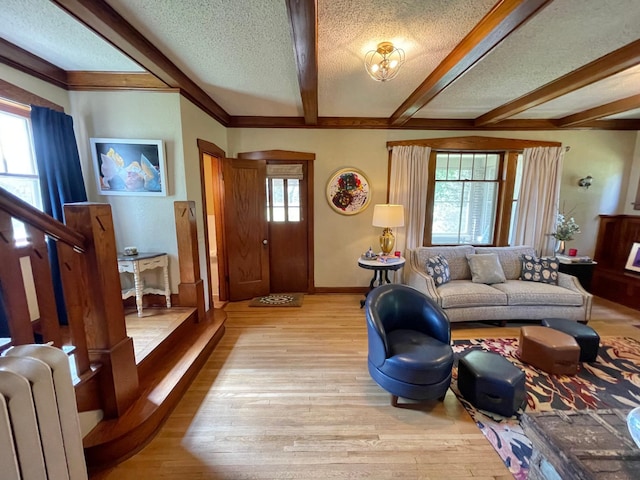 living room with radiator, beamed ceiling, ornamental molding, a textured ceiling, and light wood-type flooring