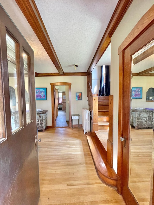 hallway featuring light hardwood / wood-style floors, radiator heating unit, beamed ceiling, a textured ceiling, and ornamental molding