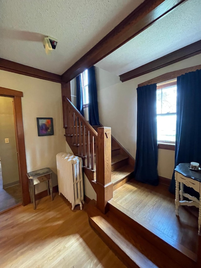 stairs with wood-type flooring, radiator, a textured ceiling, and a wealth of natural light