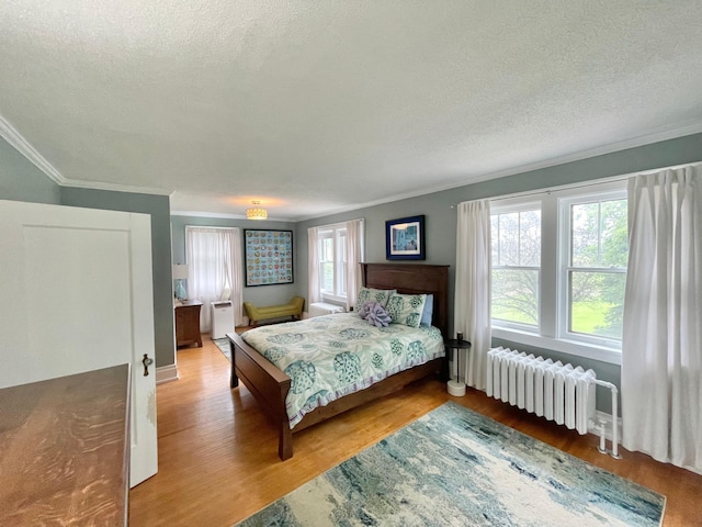 bedroom with radiator, wood-type flooring, crown molding, and a textured ceiling