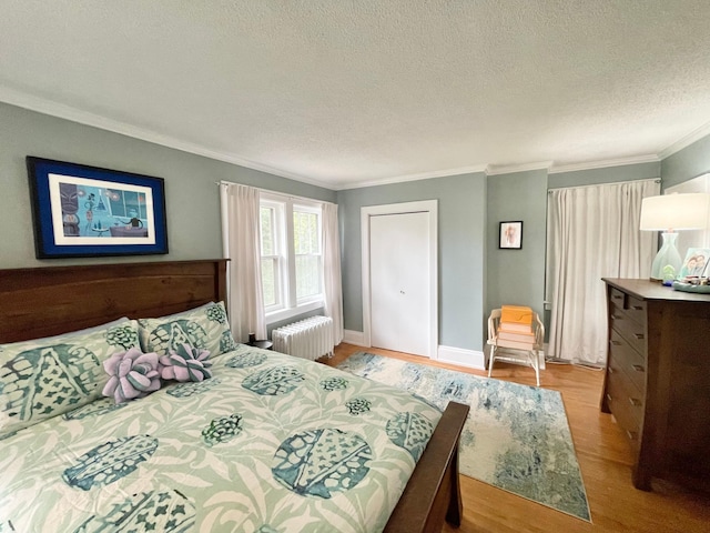 bedroom featuring a textured ceiling, light hardwood / wood-style flooring, ornamental molding, and radiator heating unit