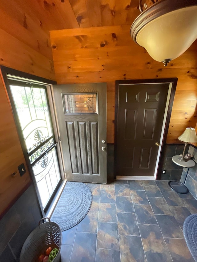 foyer featuring wooden walls and dark tile patterned floors