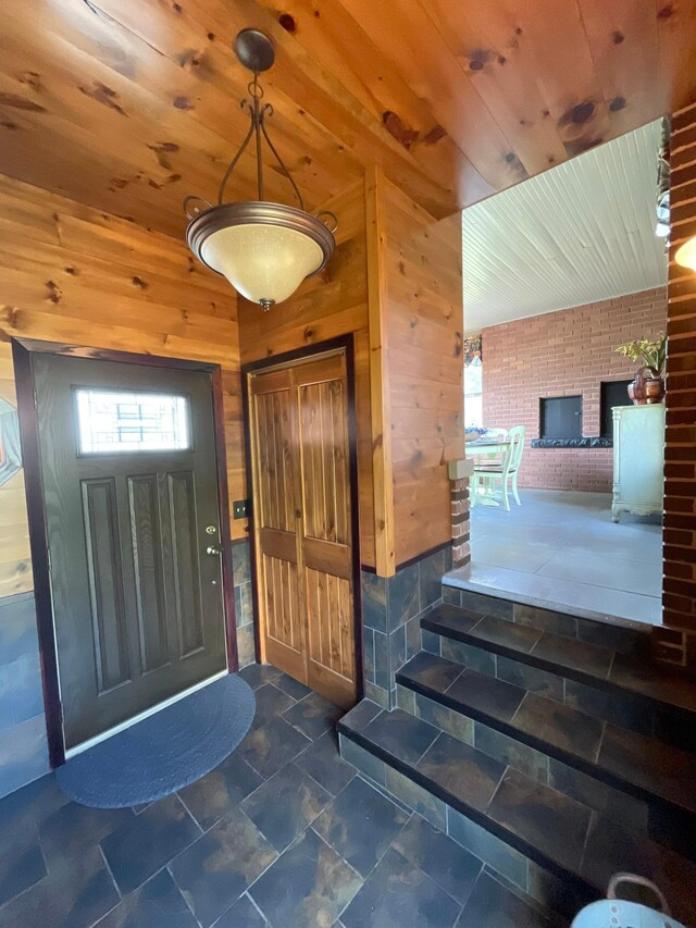 entryway with brick wall, a brick fireplace, wood ceiling, and wood walls