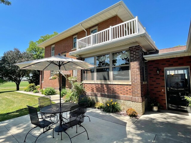 38364 200th St, Springfield, MN 56087 - rear view of property with a balcony, outdoor dining area, a patio, brick siding, and a lawn
