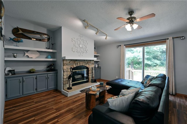 living room featuring a stone fireplace, a textured ceiling, ceiling fan, and dark hardwood / wood-style flooring