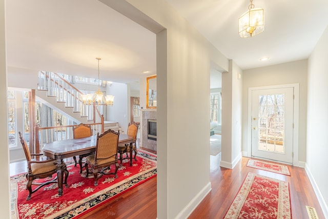 dining area featuring visible vents, baseboards, a tiled fireplace, wood finished floors, and a notable chandelier