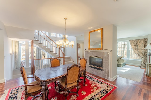 dining area featuring a tiled fireplace, stairway, a notable chandelier, and wood finished floors