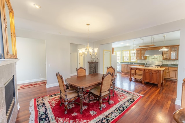 dining room with baseboards, dark wood-type flooring, a chandelier, and a fireplace