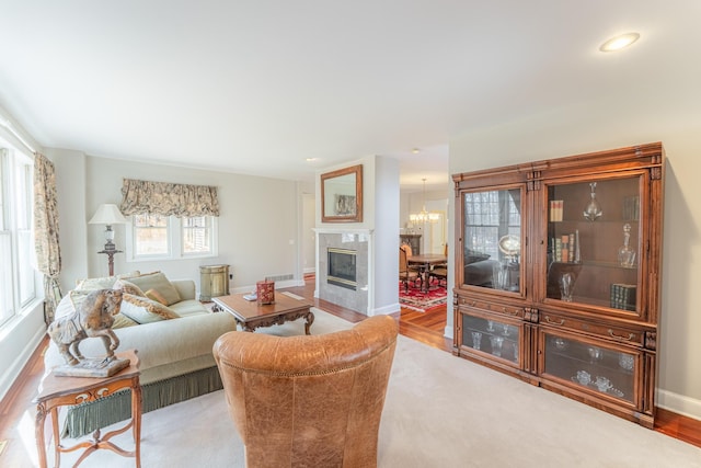 living area with visible vents, wood finished floors, a high end fireplace, an inviting chandelier, and baseboards