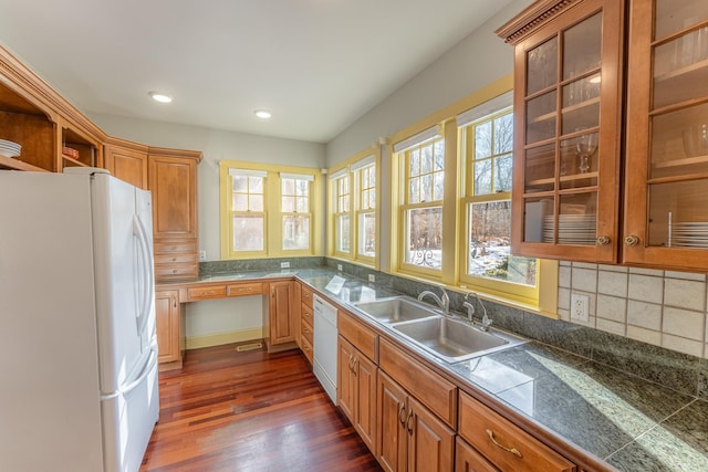 kitchen with a sink, tasteful backsplash, dark wood finished floors, white appliances, and glass insert cabinets